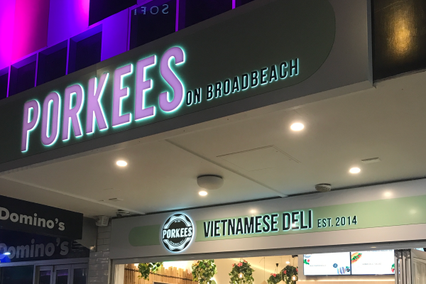glowing pink letters with green background installed to the shopfront of a restaurant
